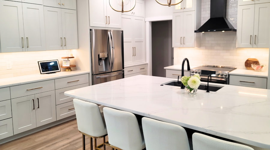 White uncluttered kitchen with mostly clear countertops. White cabinets, white counters, and white kitchen stools. Gold and black hardware.