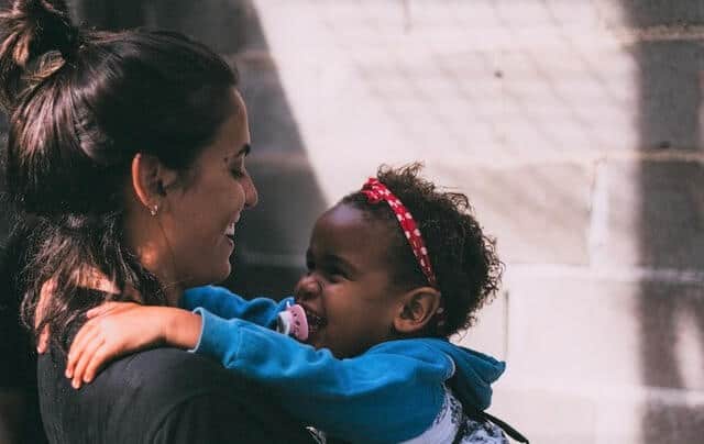Mom smiling and hugging a toddler girl.