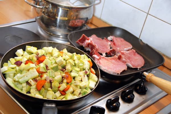 Stove top with chopped zucchini in one pan and pork chops in the other. | meal planning schedule