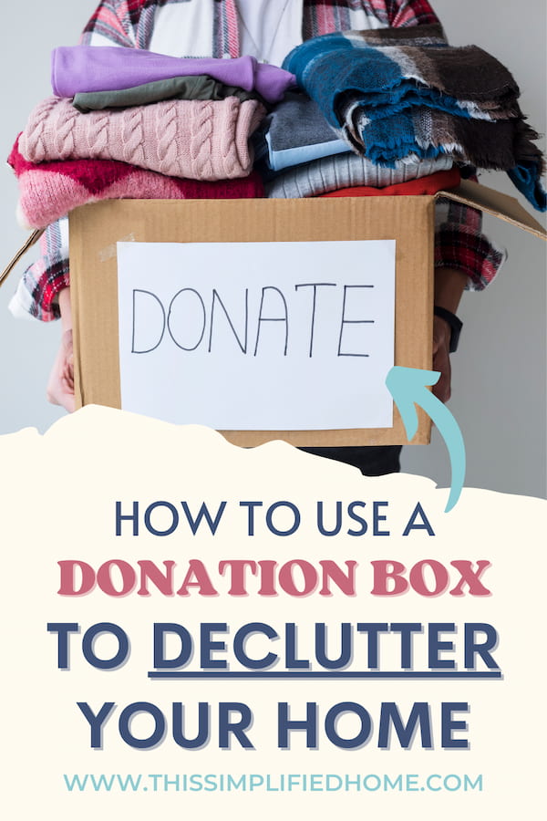 Person holding a box with DONATE written on the front. Box is filled with clothing.
