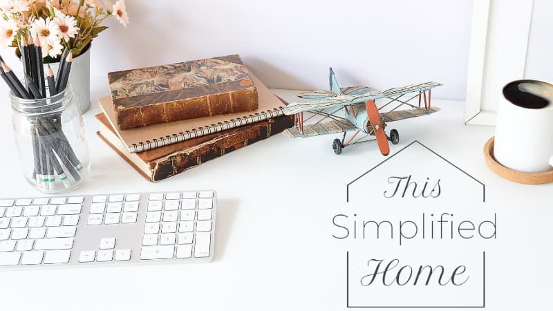 Clean and tidy desk with a keyboard, jar of pencils, antique books, and an antique toy airplane, with the This Simplified Home logo in the corner.