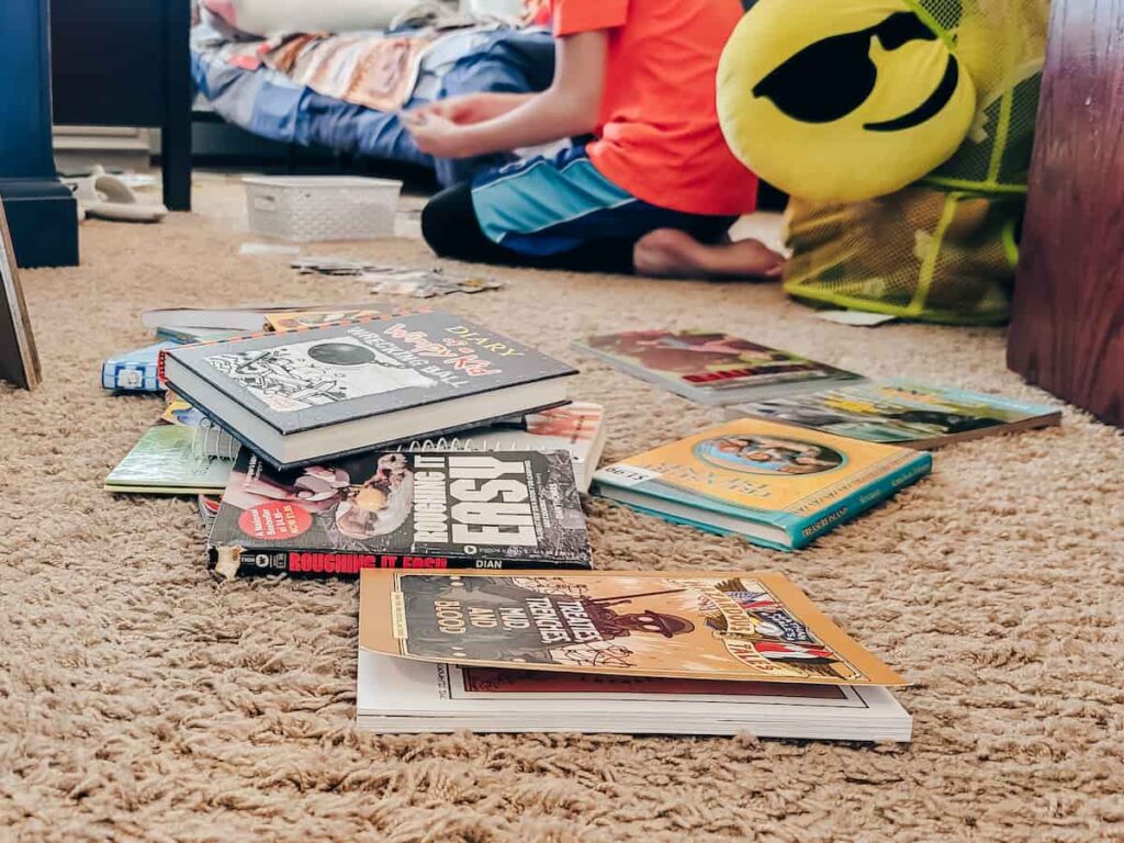 Kids chapter books on a messy bedroom floor. Neck down image of a child learning to declutter.